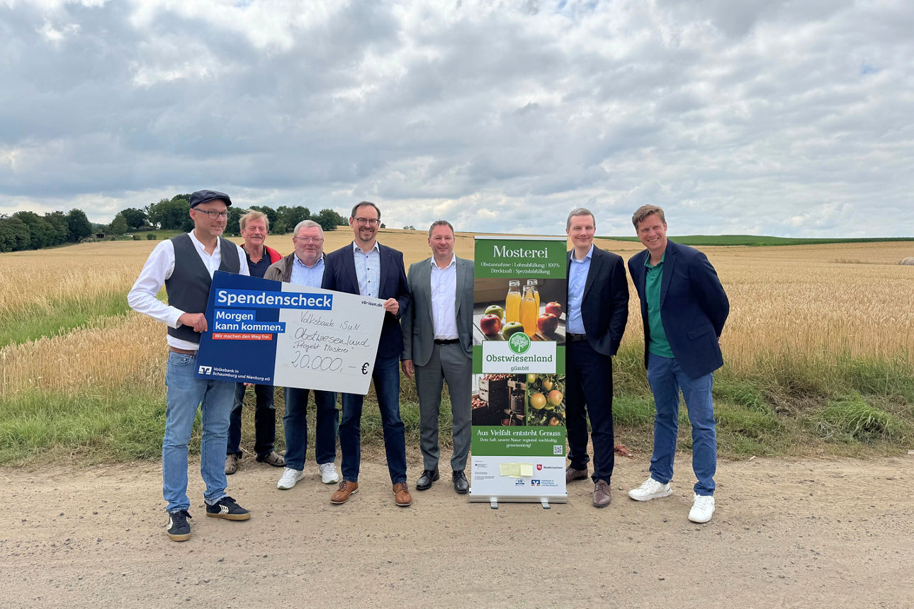 Eine Gruppe Menschen stehen vor einem Acker und halten Projektschilder in der Hand.