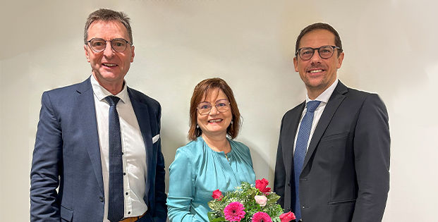 Zwei Männer stehen neben einer Frau, die einen Blumenstrauß in der Hand hält.