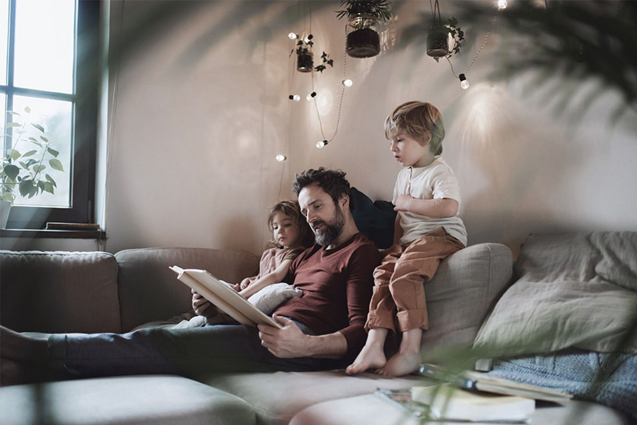 Ein Vater liest seinen zwei Kindern etwas auf der Couch vor