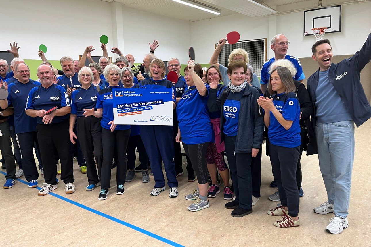 Zahlreiche Vereinsmitglieder jubeln mit einem Spendenscheck und Tischtenniskellen in der Hand
