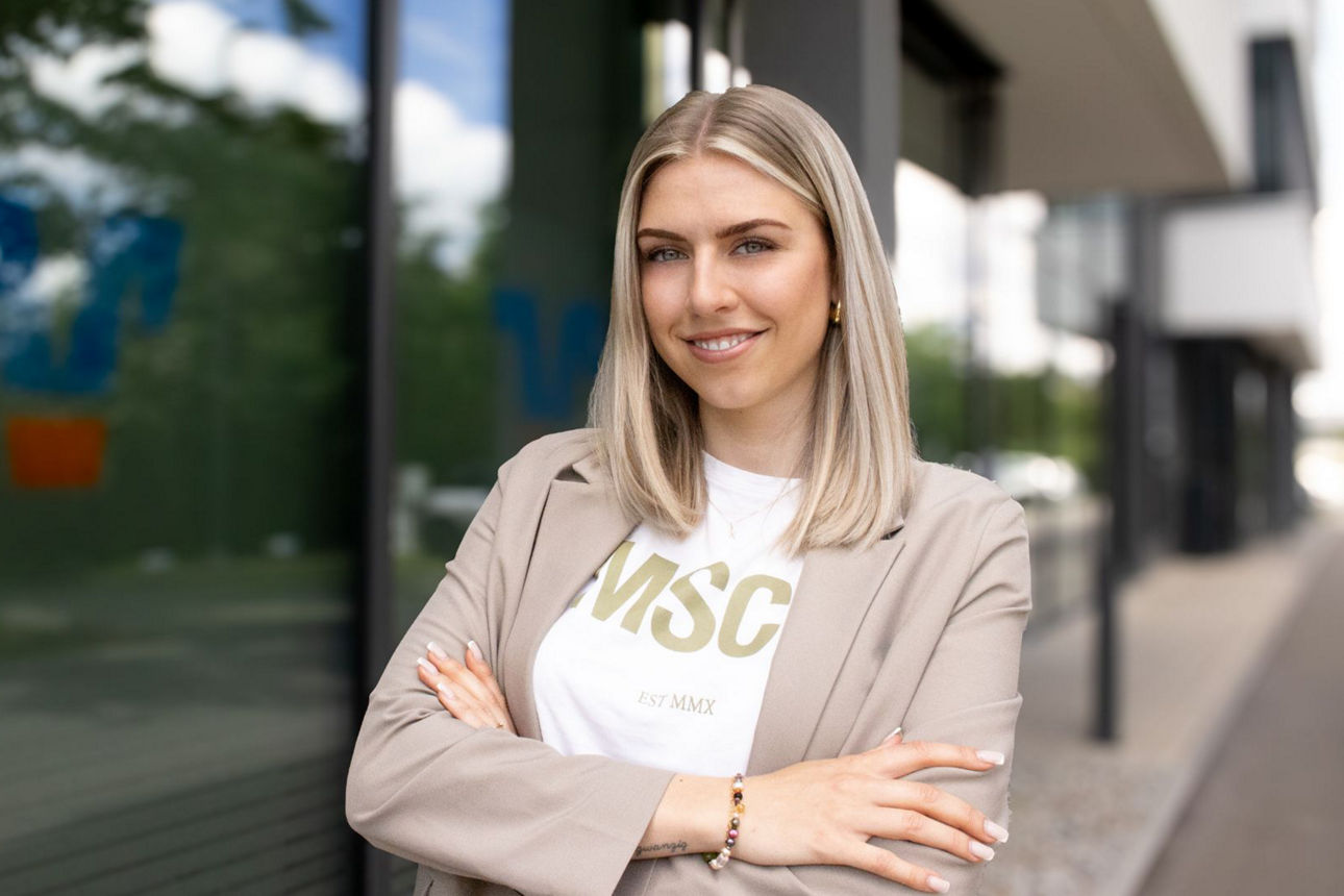 Junge Frau steht lächelnd vor einem Gebäude