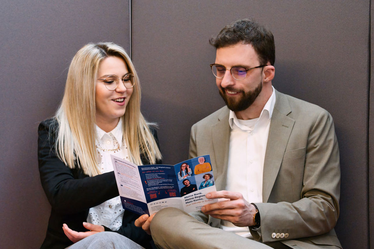 Lächelnde Frau und Mann sitzend und schauen sich einen Flyer an