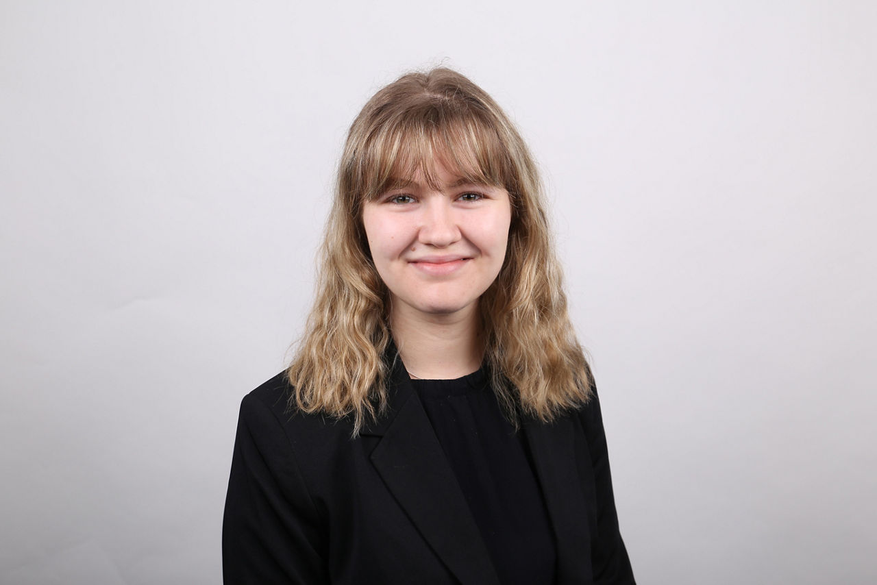 Mitarbeiterin der Bank, Ronja Buckel, steht vor weißer Wand und lächelt in die Kamera