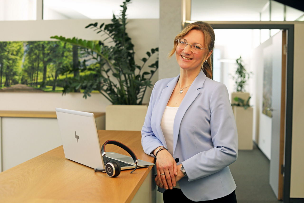 Mitarbeiterin der Bank, Carina Eilert, lehnt am Bürothresen und lächelt in die Kamera