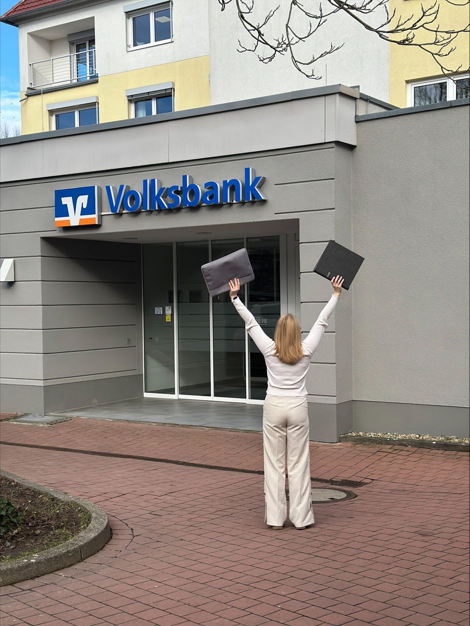 Eine junge Frau streckt vor dem Eingang der Volksbank die Hände in die Höhe.