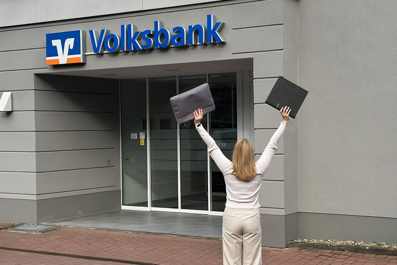 Eine junge Frau streckt vor dem Eingang der Volksbank die Hände in die Höhe.