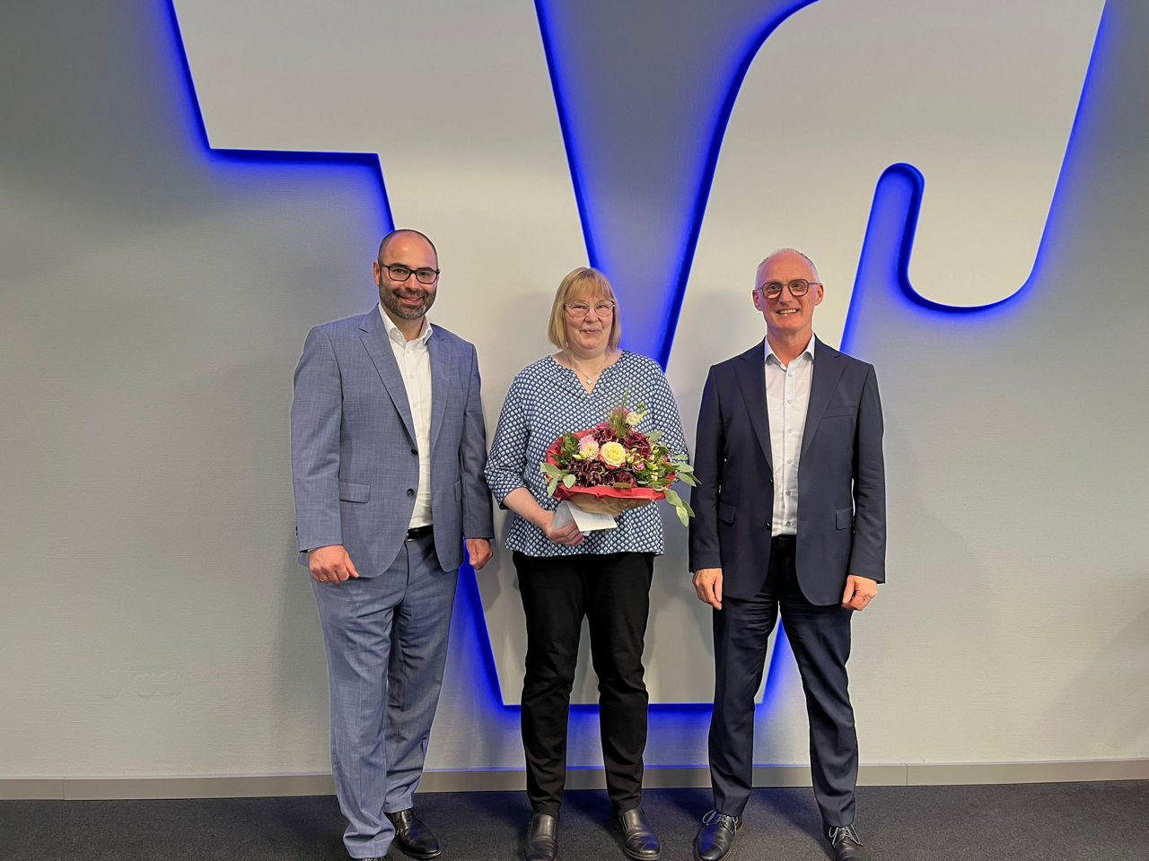 Zwei Herren und eine Dame vor einem Volksbank Logo in einer Geschäftsstelle