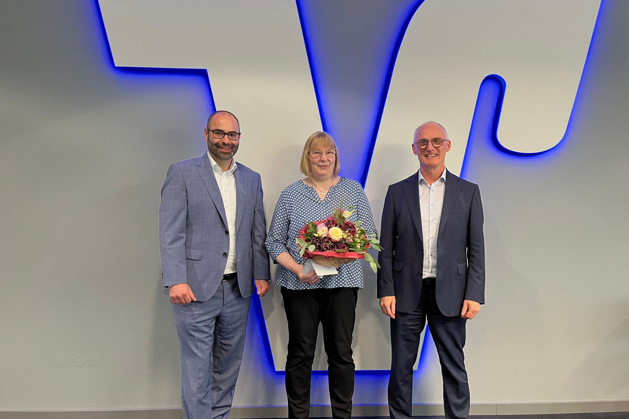 Zwei Herren und eine Dame vor einem Volksbank Logo in einer Geschäftsstelle