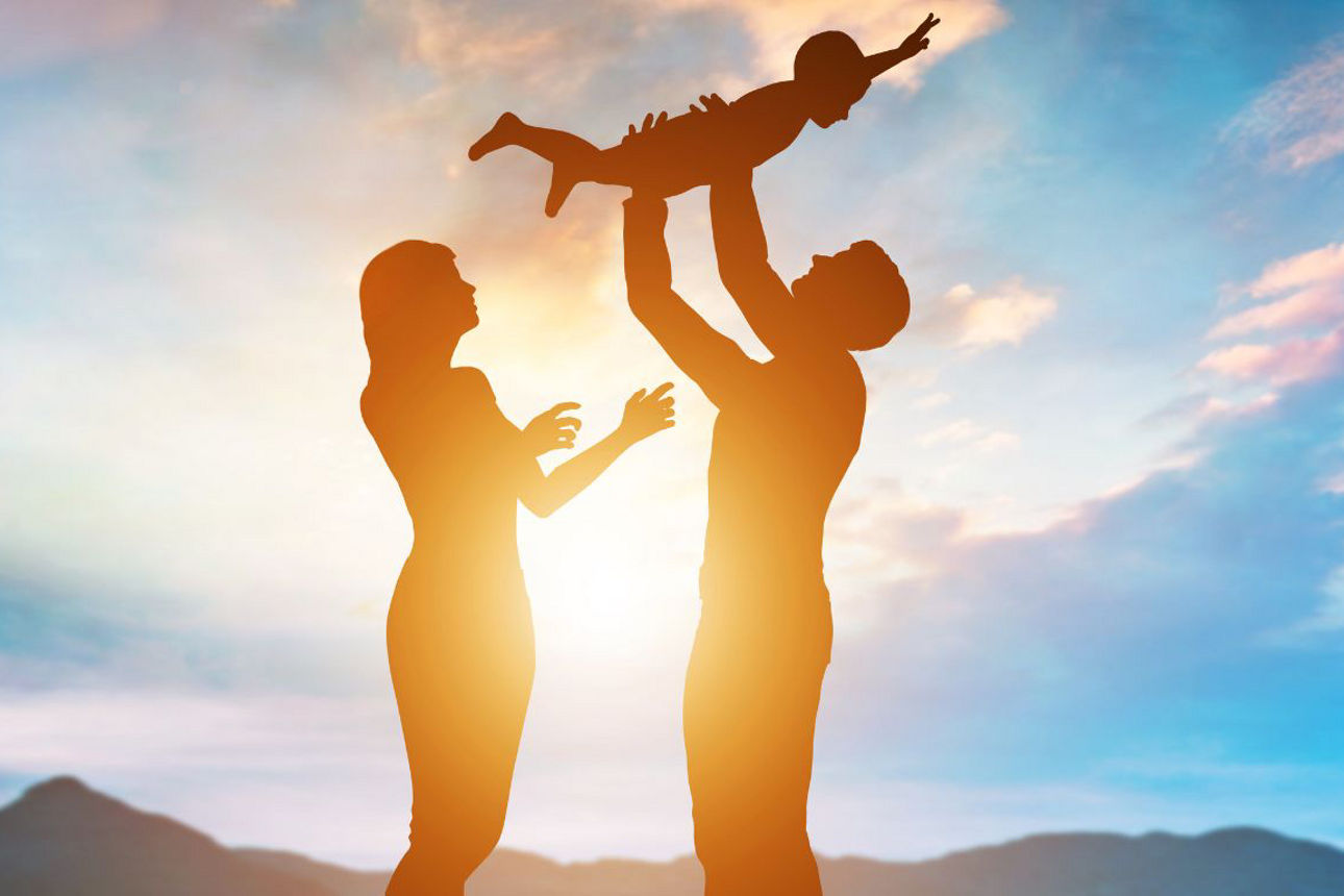 Elternpaar schauen glücklich ihr gemeinsames Baby an, welches der Mann in den Armen hält.