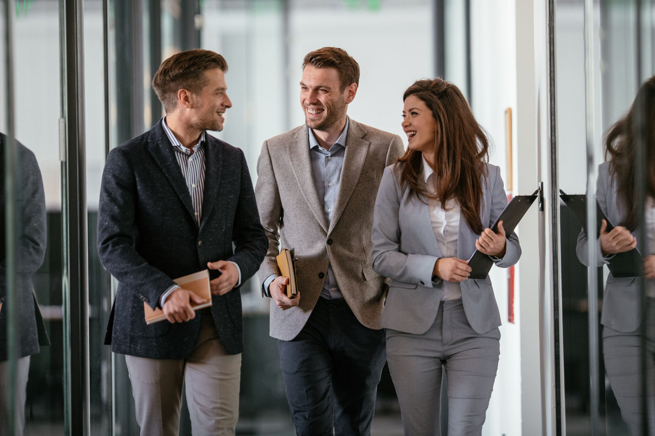 Zwei Männer und eine Frau in Business-Kleidung lachend im Gespräch