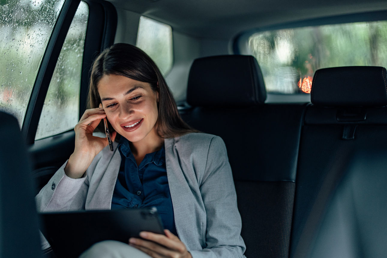 Eine Frau sitzt im Auto an einem Tabelett und telefoniert