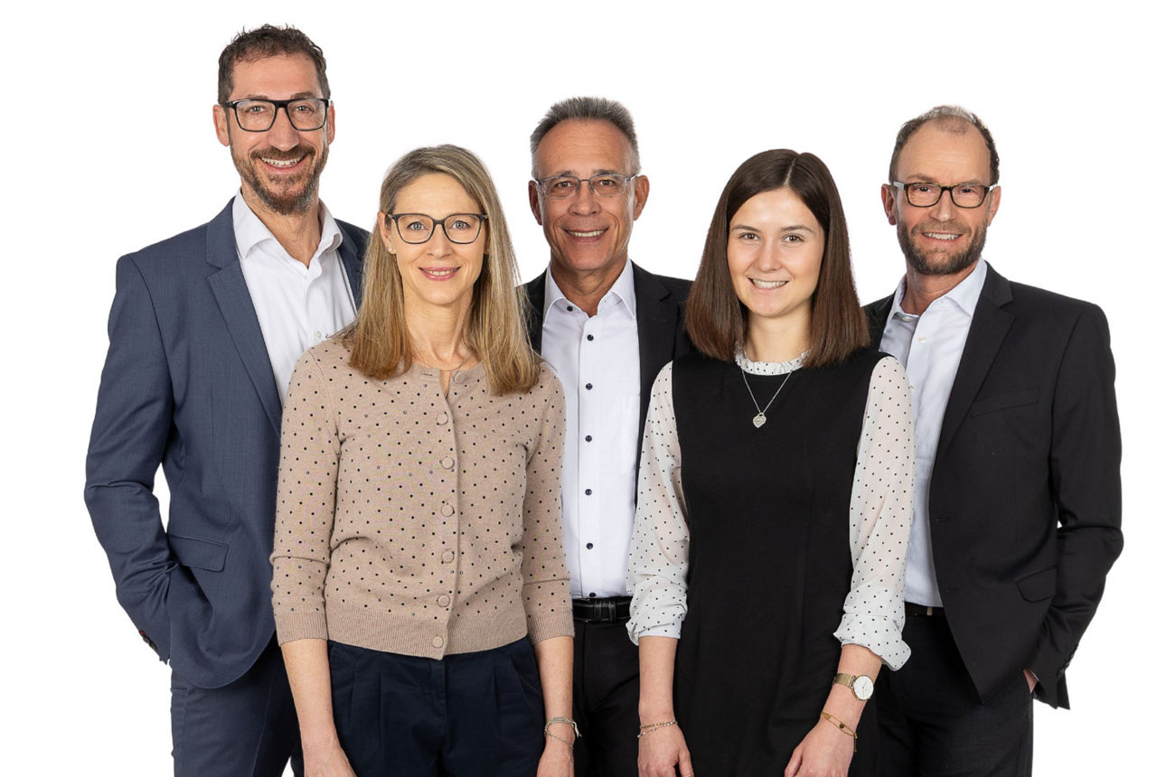 Fünf Mitarbeitende des Immobilien-Teams in Businesskleidung vor hellem Hintergrund.