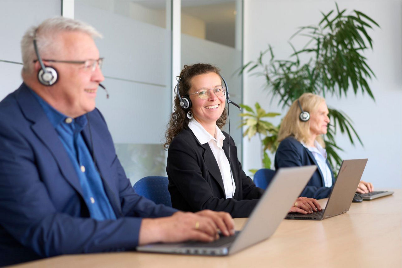 Drei Personen in einem Konferenzraum mit Headsets und Laptops