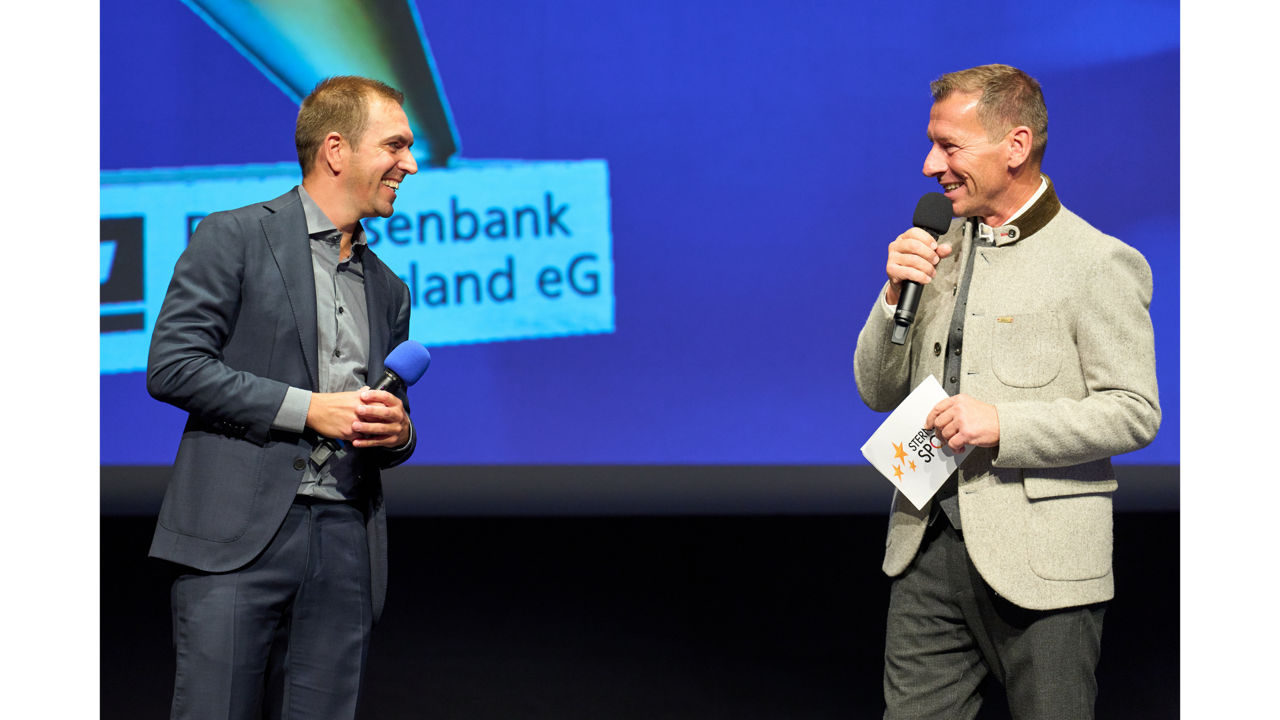 Zwei Männer sind auf einer Bühne im Gespräch.