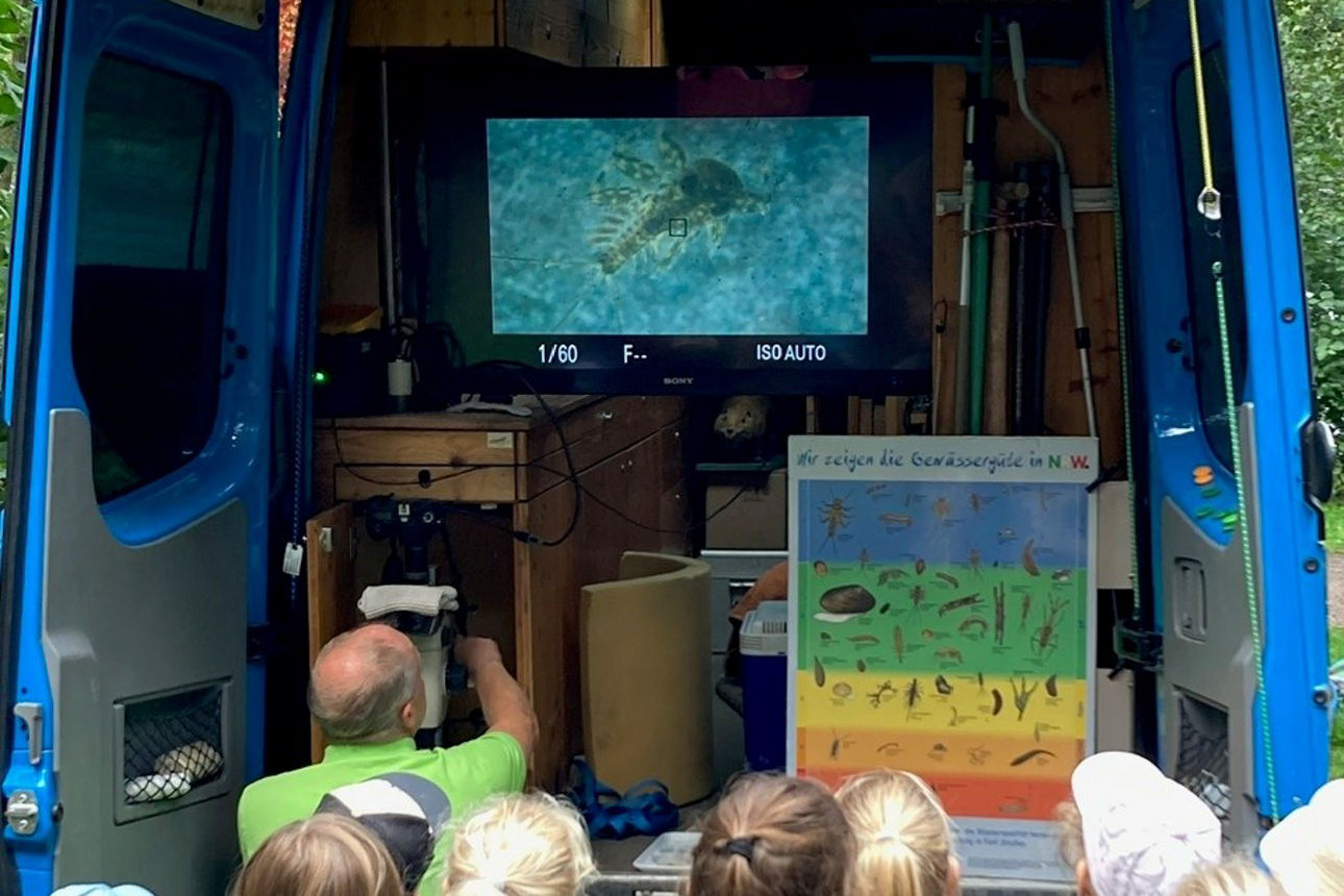 Kinder beobachten im Rumpelmobil die kleinen Würmer auf einem großen Bildschirm