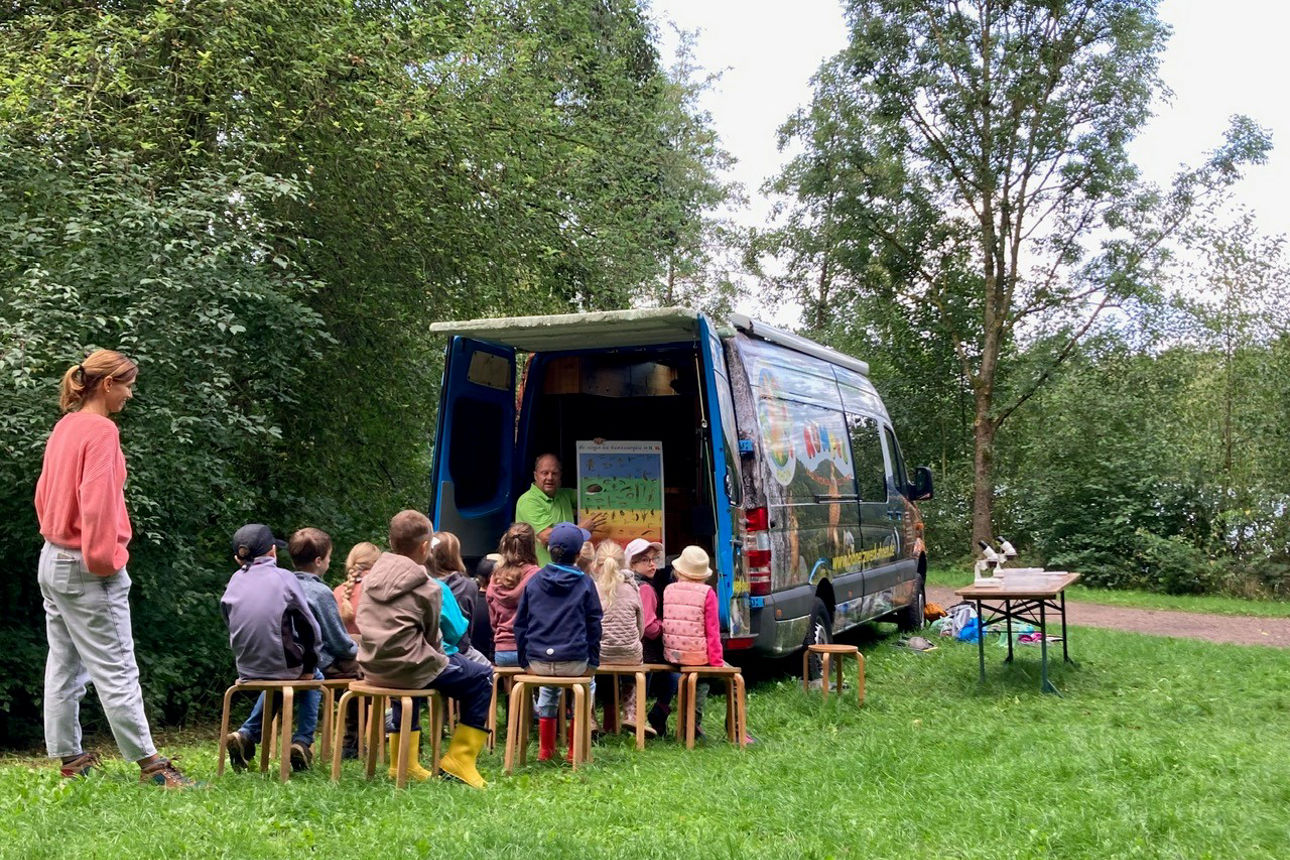 Kinder von hinten am Rumpelmobil auf einer grünen Wiese
