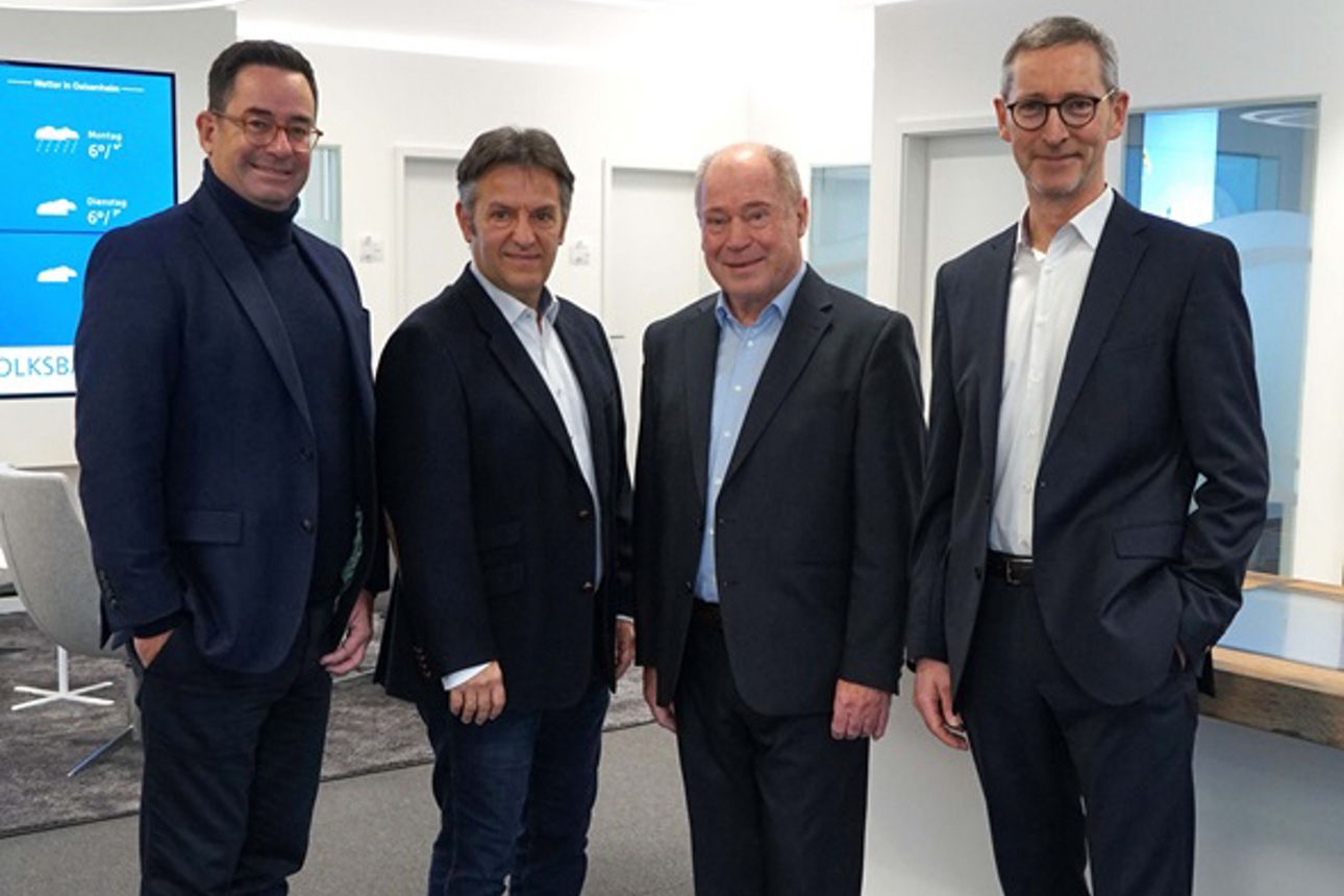 Vier Männer mittleren Alters im Anzug stehen in einem modernen Bürogebäude