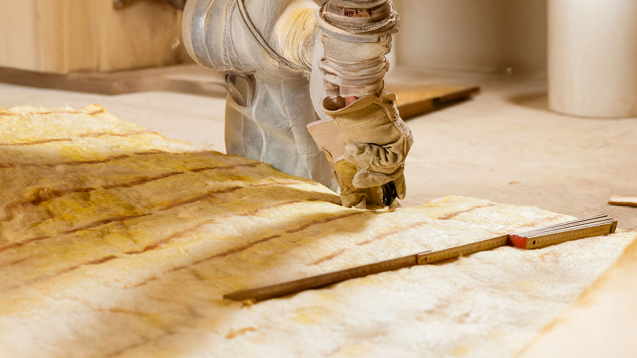 Eine Handwerkerhand mit Arbeitshandschuh beim Zuschneiden von Dämmmaterial