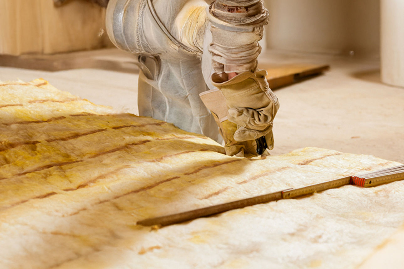 Eine Handwerkerhand mit Arbeitshandschuh beim Zuschneiden von Dämmmaterial