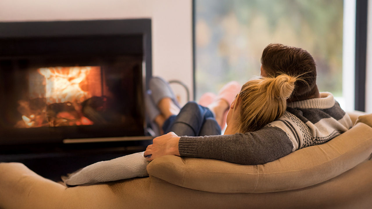 Ein Paar kuschelt auf einer Couch und schaut auf ein Kaminfeuer