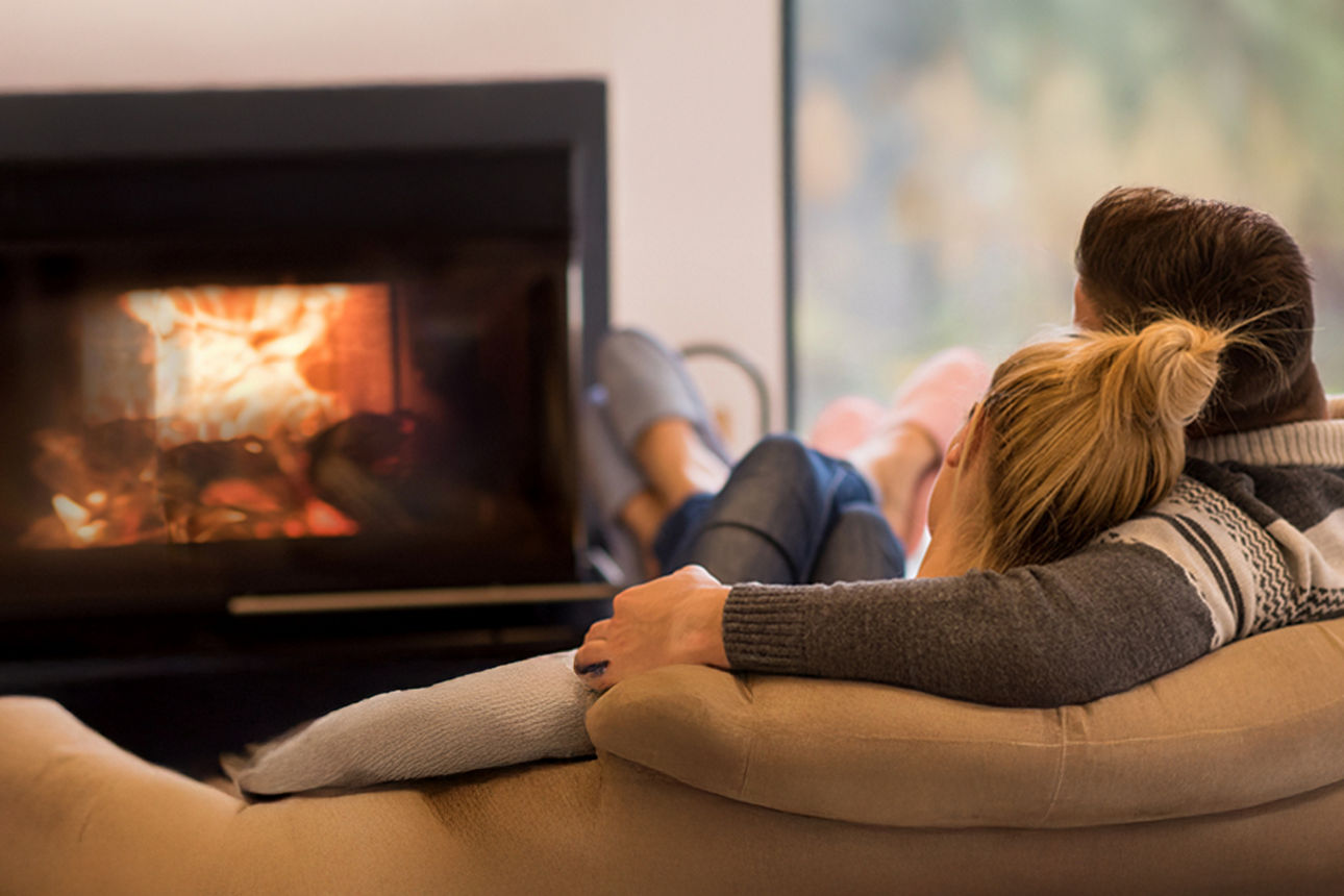 Ein Paar kuschelt auf einer Couch und schaut auf ein Kaminfeuer