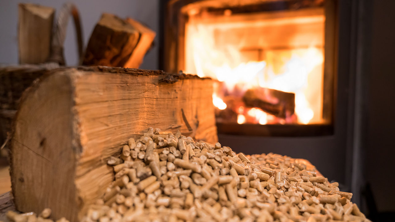 Ein Häufchen Holzpellets, im Hintergrund ein Pelletofen