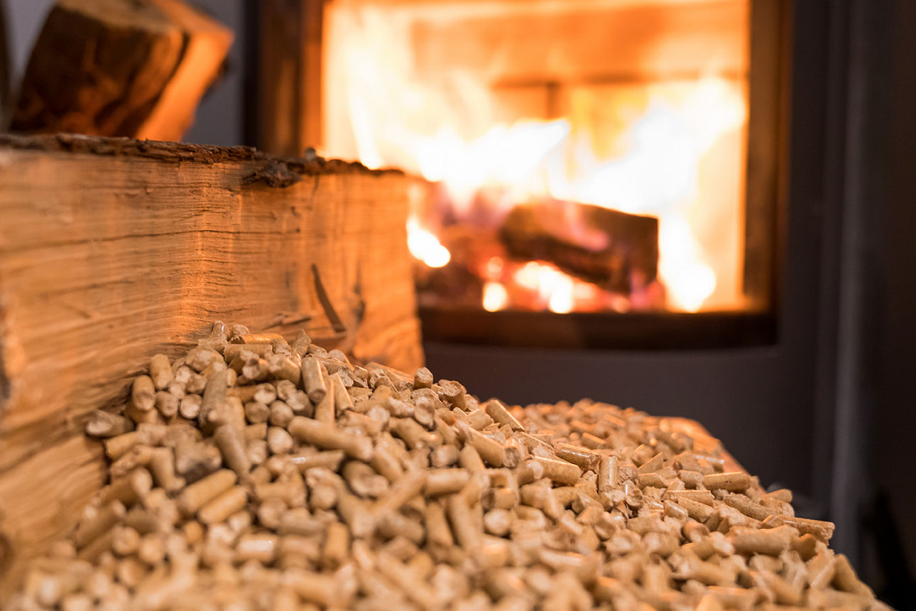 Ein Häufchen Holzpellets, im Hintergrund ein Pelletofen
