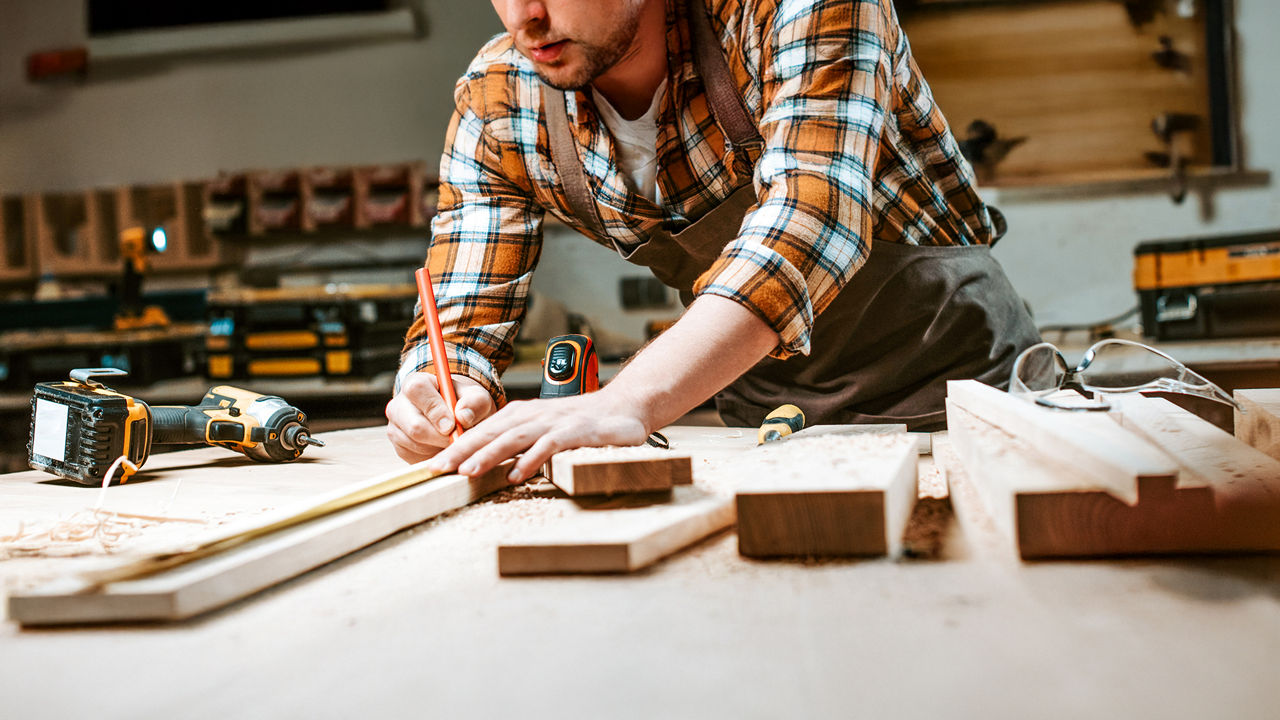 Ein Heimwerker markiert mit einem Bleistift ein Holzbrett