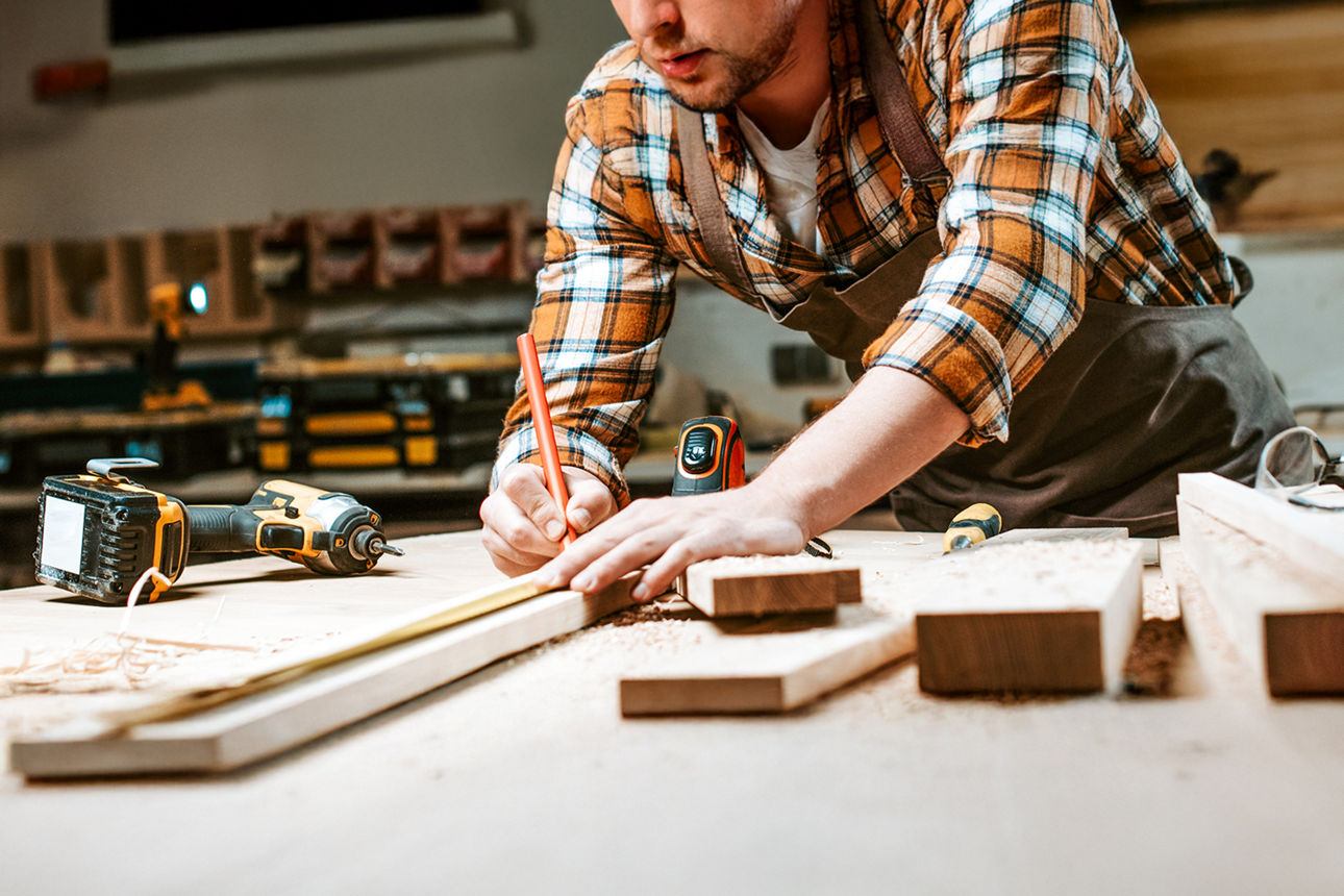 Ein Heimwerker markiert mit einem Bleistift ein Holzbrett