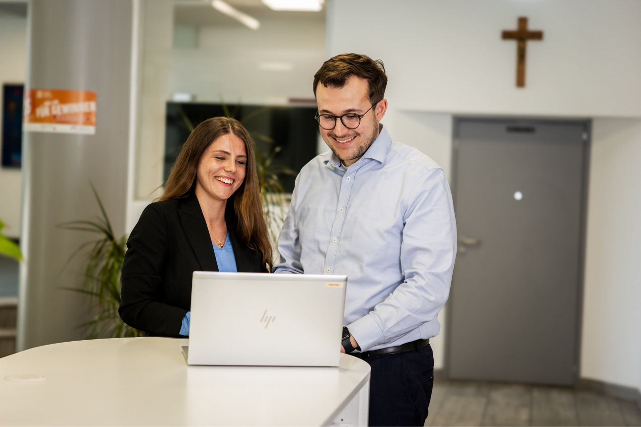 Mann und Frau stehen an einem Tresen und schauen in einen Laptop