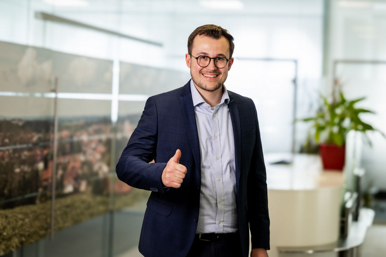 Mann steht im Eingangsbereich der Bank, lächelt in die Kamera und hebt einen Daumen hoch