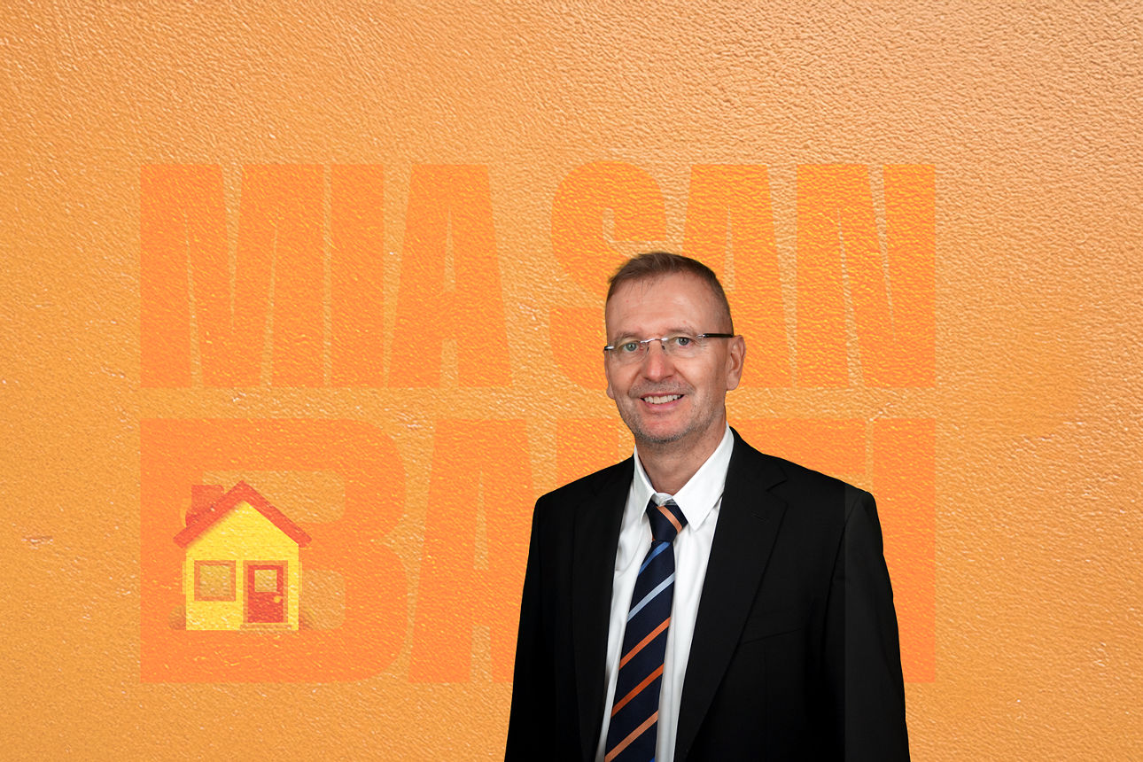 Ein Mann steht vor einem orangen Hintergrund.