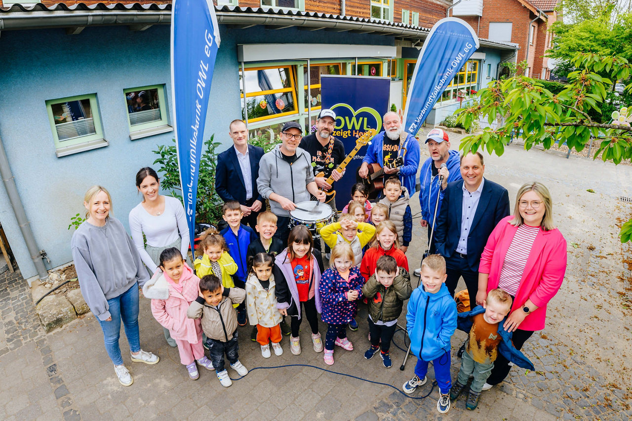 Musiker der Band „Randale“ stehen inmitten von strahlenden Kindern, Erzieherinnen der Kita Kunderbunt und Mitarbeitern der VerbundVolksbank OWL eG.