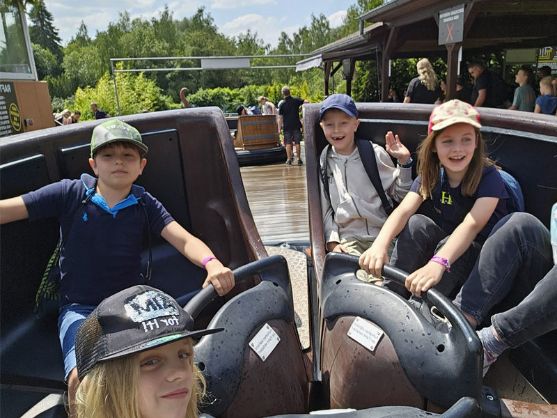 Fünf Kinder sitzen in einemrunden Holzboot einer Wildwasserbahn. 