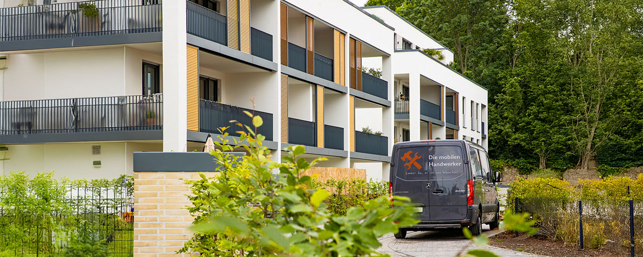 Mehrfamilienhaus mit einer Einfahrt in der ein Firmenwagen steht