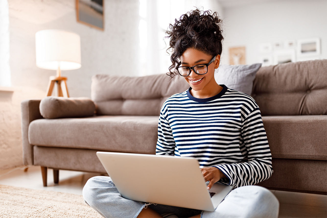 Frau sitzt mit Laptop auf dem Schoß vor einem Sofa