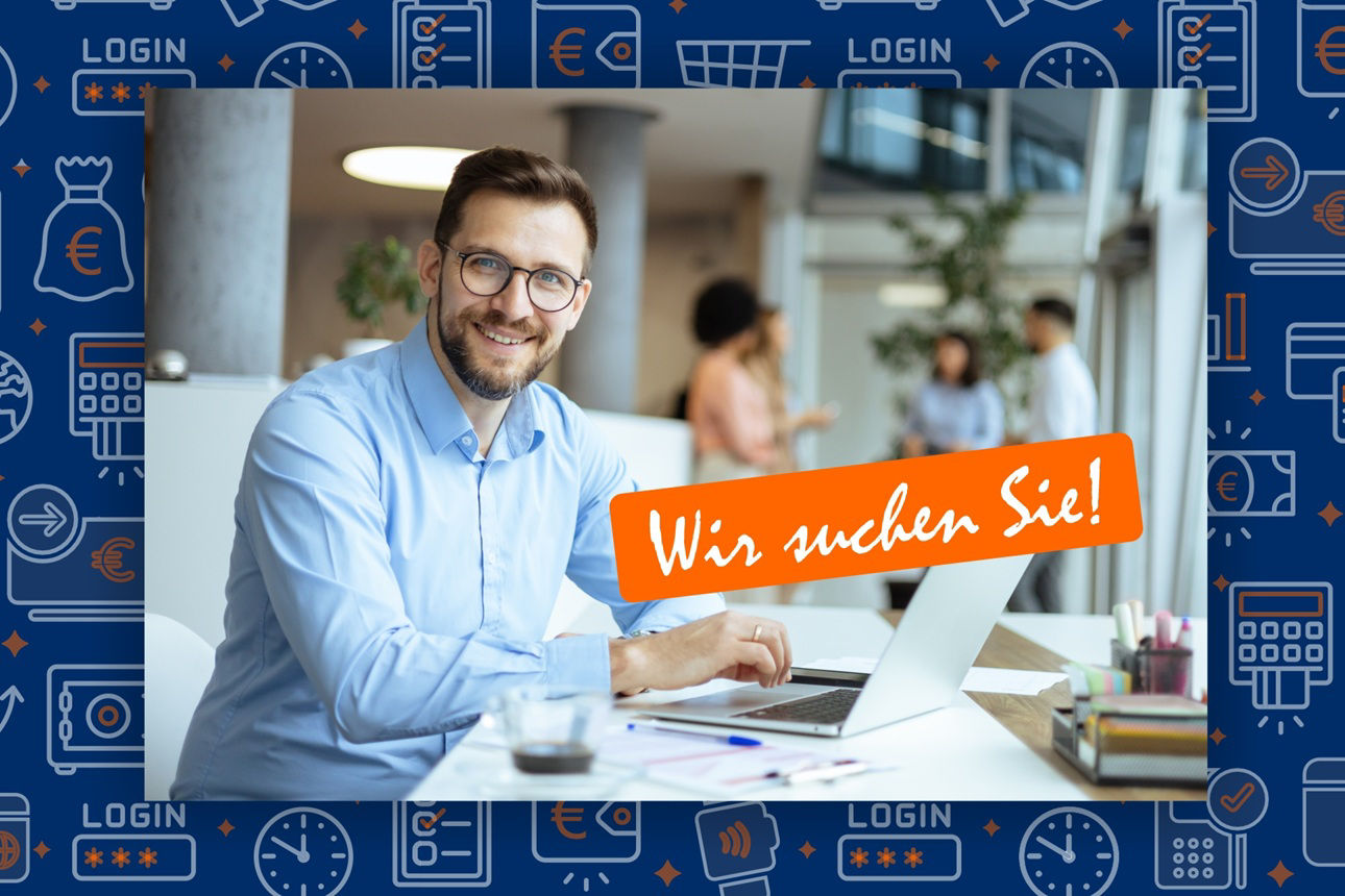 Junger Mann sitzt an einem Schreibtisch und hat einen Laptop vor sich und lächelt freundlich in die Kamera