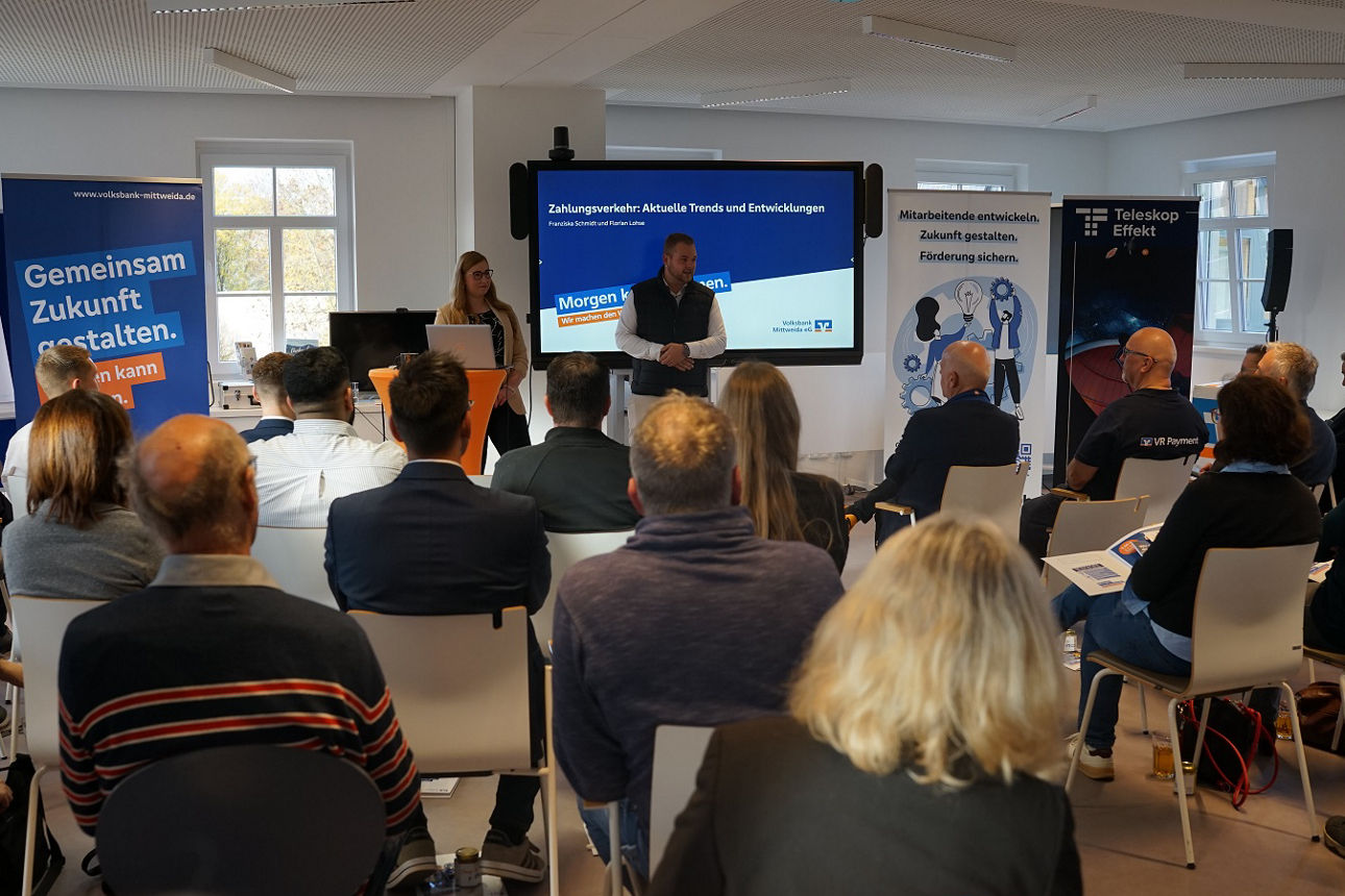 Business Frühstück 2.0: Blick in den Veranstaltungsraum von hinten, Besucher:innen sitzen und blicken zum Referenten