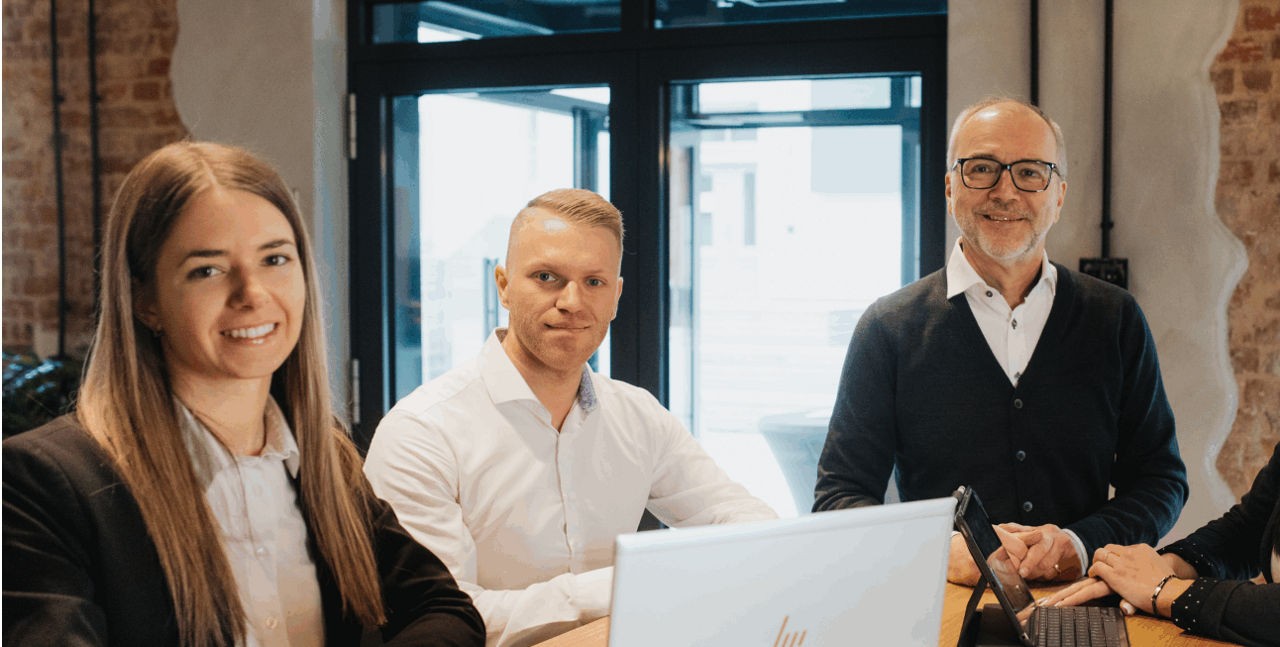 3 Mitarbeiter der Bank sitzen an einem Tisch vor dem Laptop