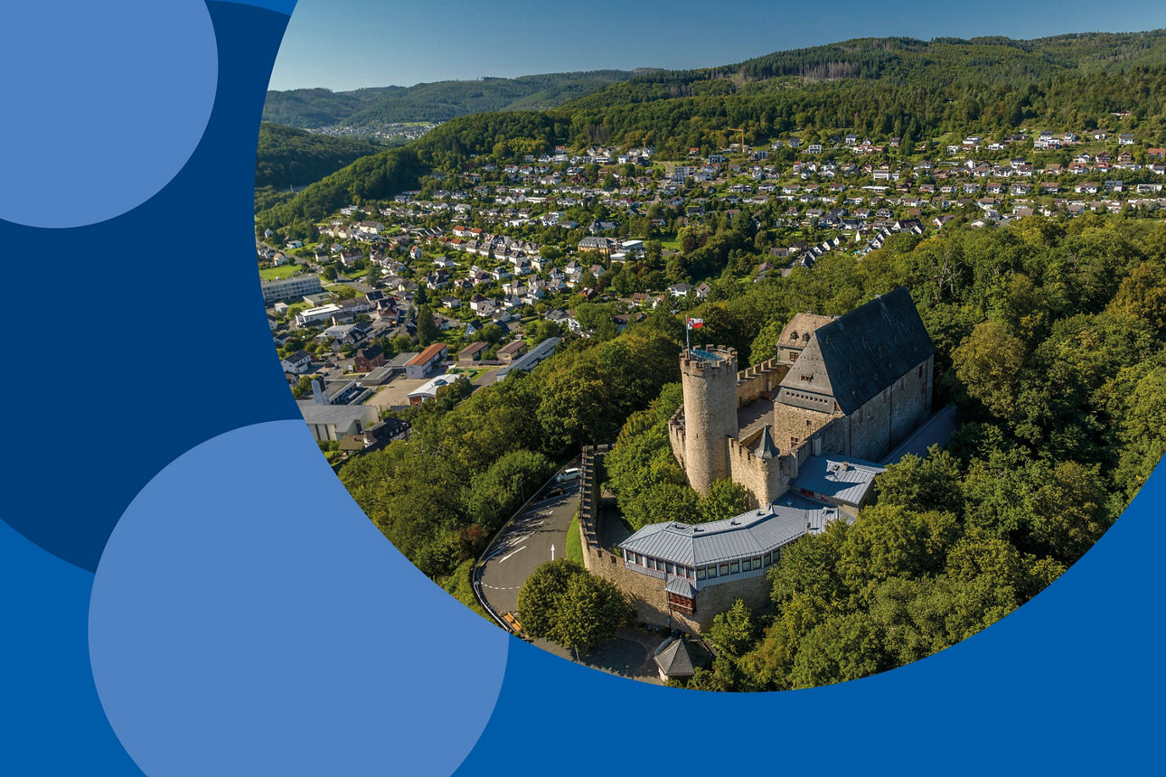 Im Vordergrund sieht man das Schloss von Biedenkopf aus der Vogelperspektive. Im Hintergrund liegt die Stadt Biedenkopf und den Wald.