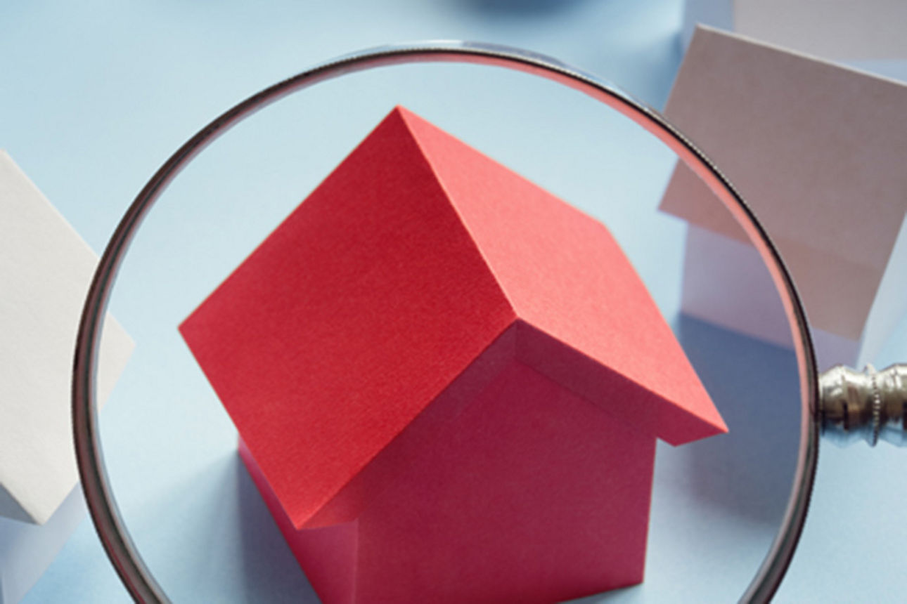 Lupe über einem roten Spielzeug-Holzhaus neben weiteren weißen Spielzeug-Holzhäsuern