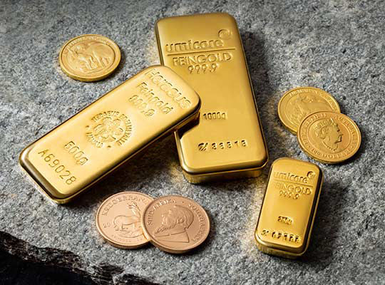 Goldmünzen und Goldbarren liegen auf einer Steinplatte