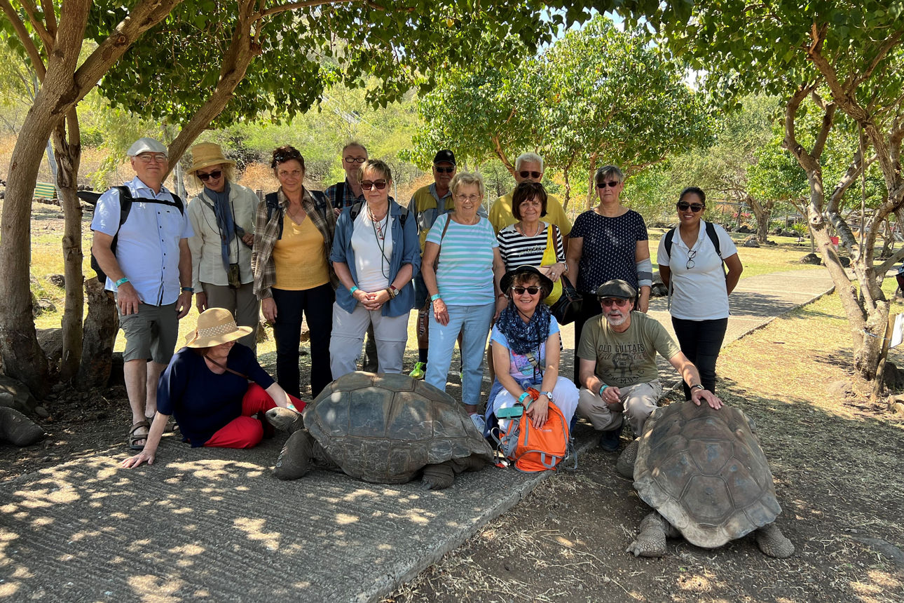 Mauritius Reisegruppe - Gruppe Menschen im Sonnenschein in Freizeitkleidung mit riesigen Schildkröten