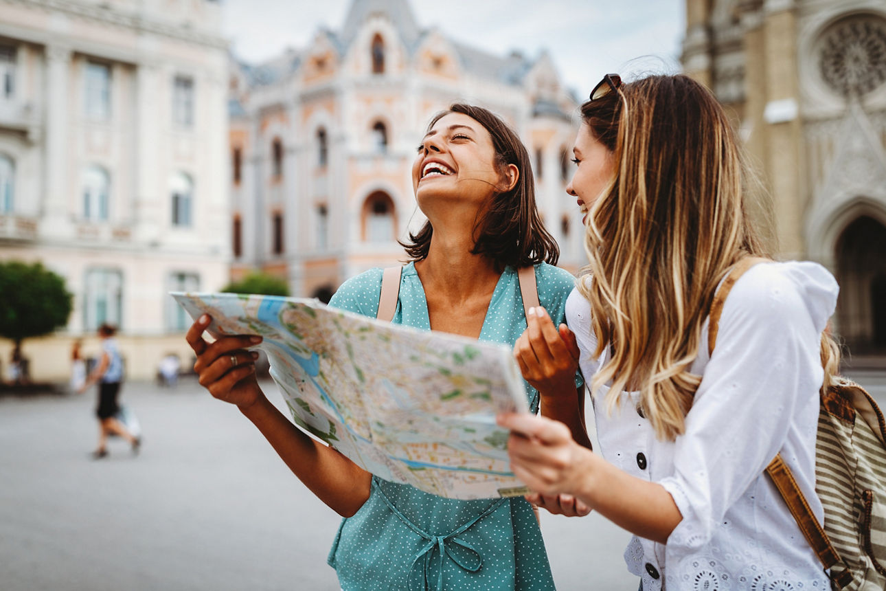 Zwei Frauen auf Städtereise halten einen Stadtplan und lachen