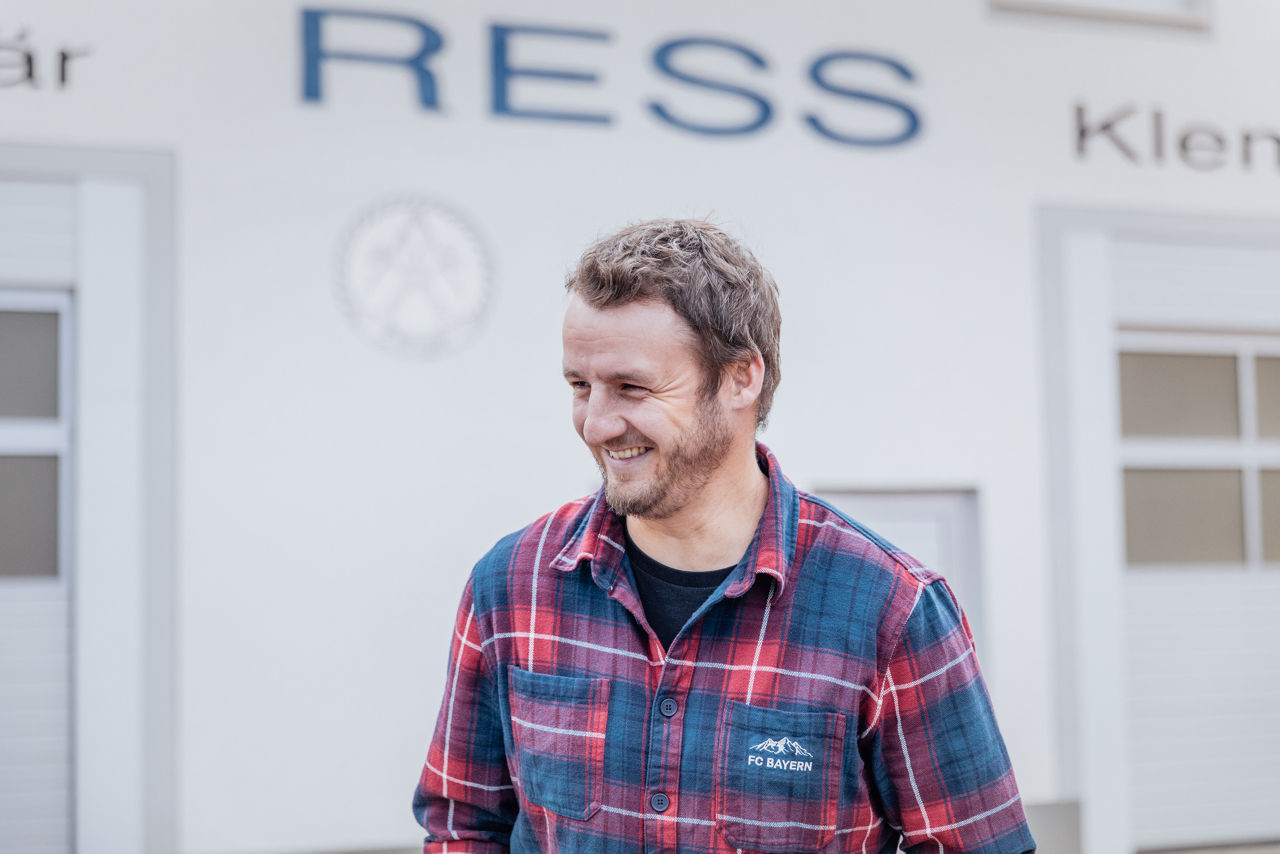 Christoph Rützel steht vor dem Firmengebäude des Sanitär‑ und Heizungsbetriebs von „Ress GmbH“. Sichtbar sind die Gebäudebeschriftung sowie der Eingangsbereich der Klempnerei und SHK‑Werkstatt