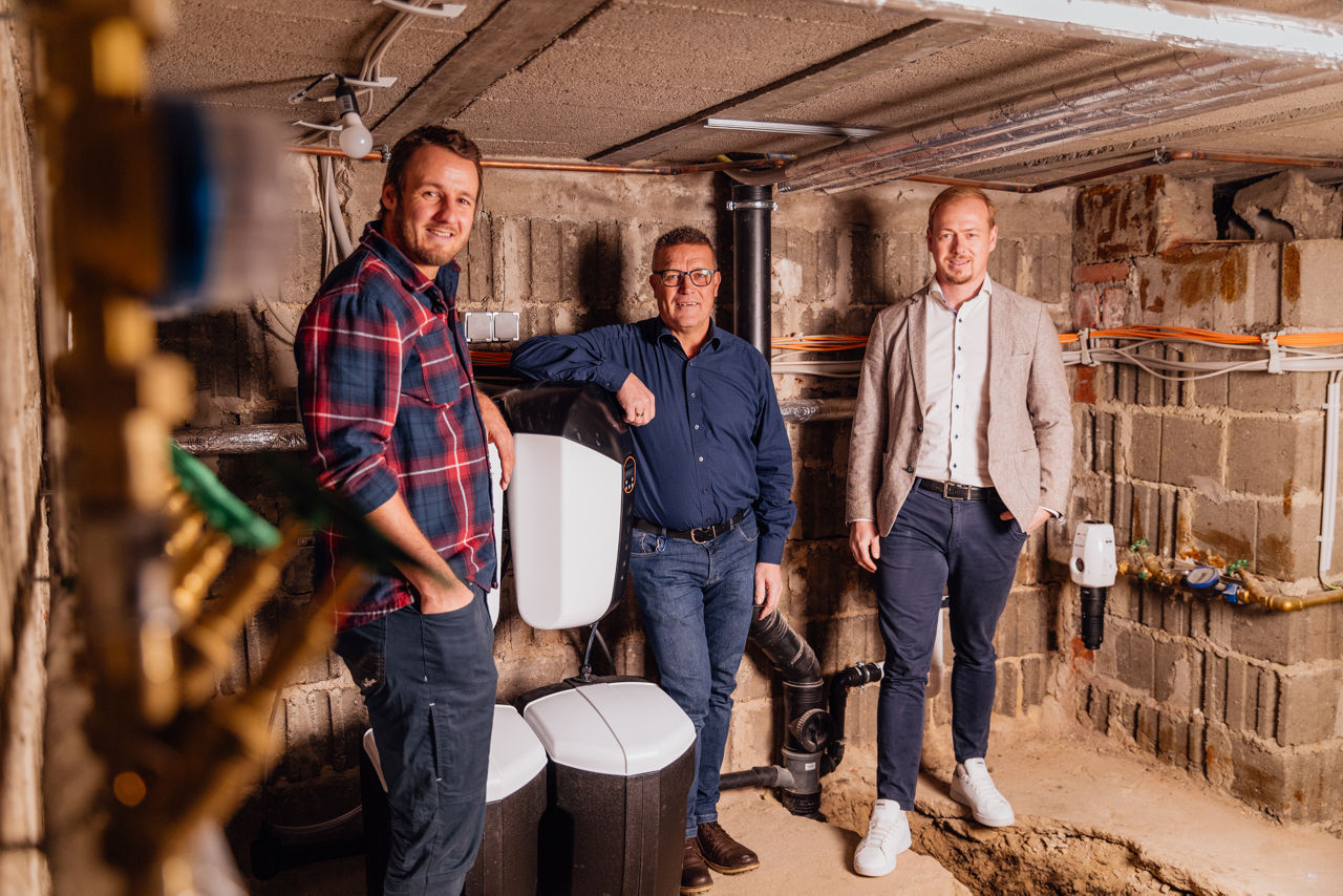 Christoph Rützel, Georg Rützel und Berater Florian Abschütz stehen im Technikraum des Sanitär‑ und Heizungsbetriebs der „Ress GmbH“. Sichtbar sind montierte Wärmetechnik‑Einheiten, Rohrleitungen sowie Installationskomponenten aus dem Sanitär‑ und Heizungsbereich