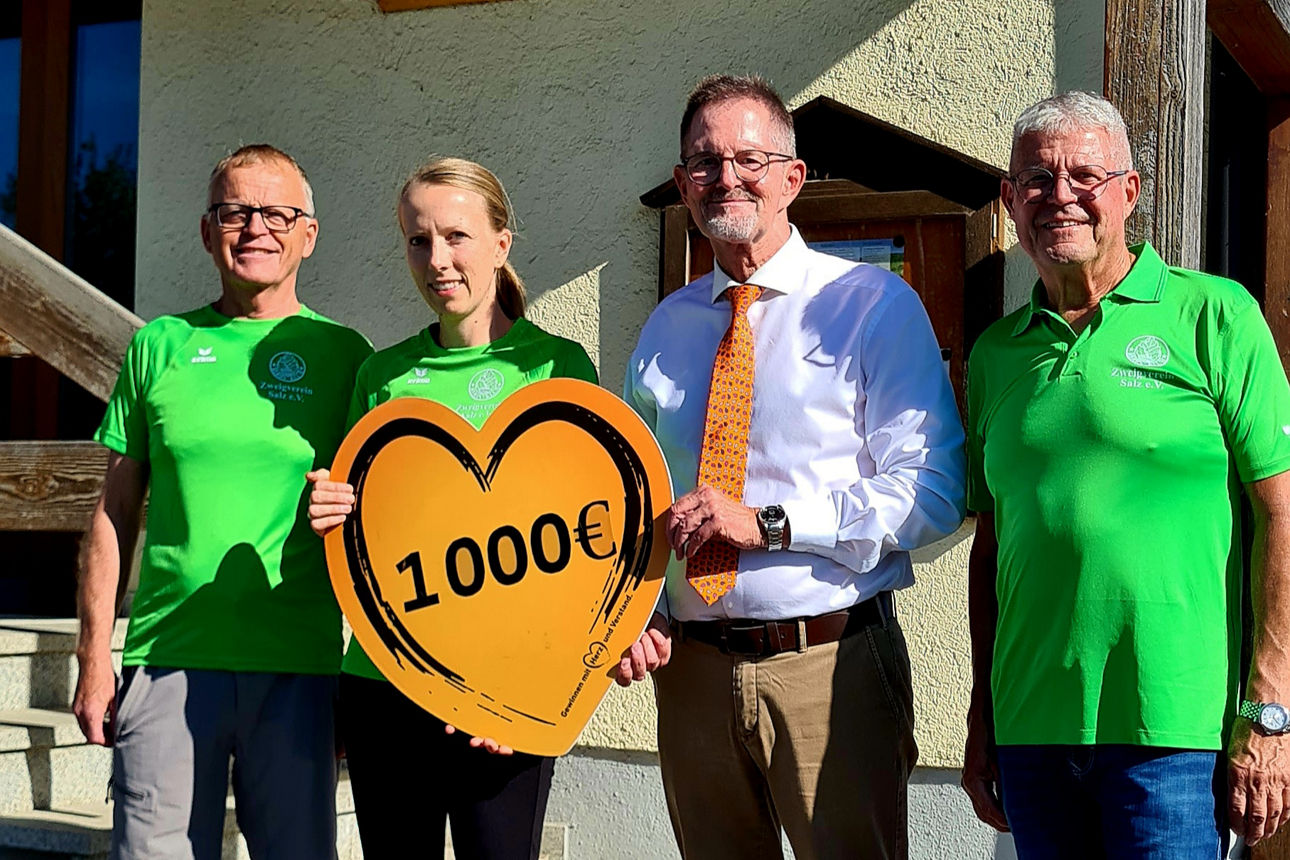 3 Männer und eine Frau stehen vor dem Gebäude des Rhönklubs. Eine Frau vom Rhönklub und ein Vertreter der Bank halten ein Herz aus orangenem Pappkarton auf dem die Spendensumme von 1.000 € steht. 