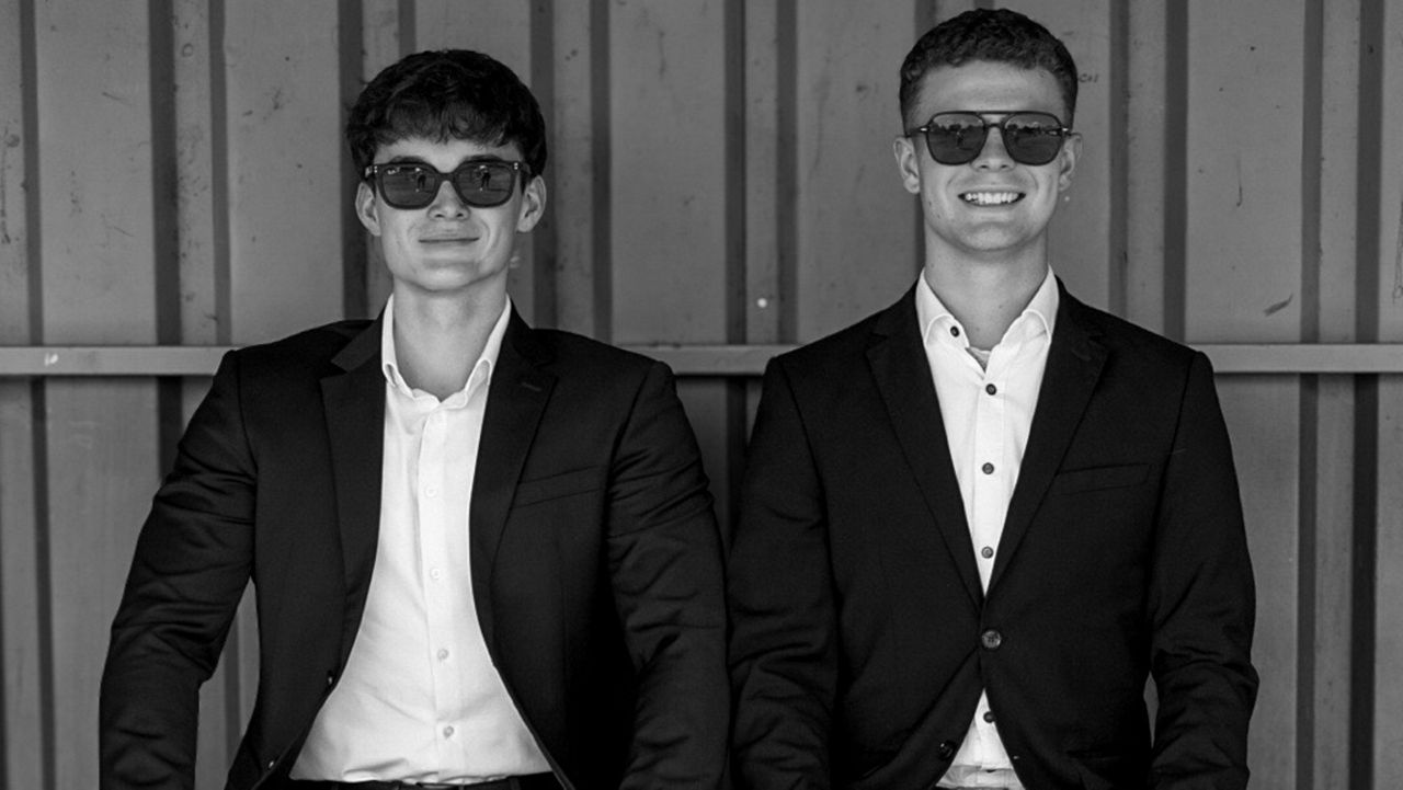 Die Moderatoren Leon und Ricci in dunklen Anzügen mit Sonnenbrillen in einer Schwarz-Weiß-Aufnahme.