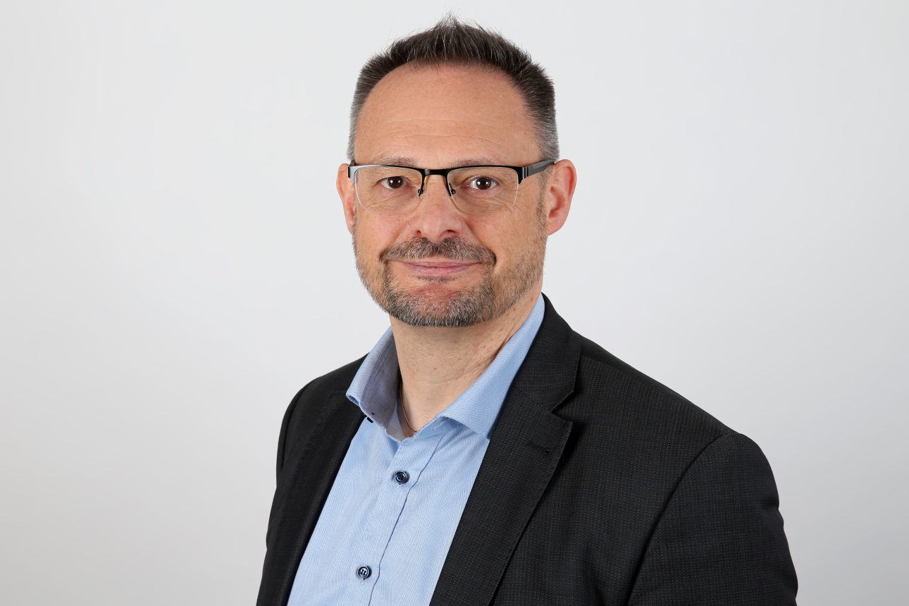 Ein lächelnder Mann in einem Anzug schaut in die Kamera.