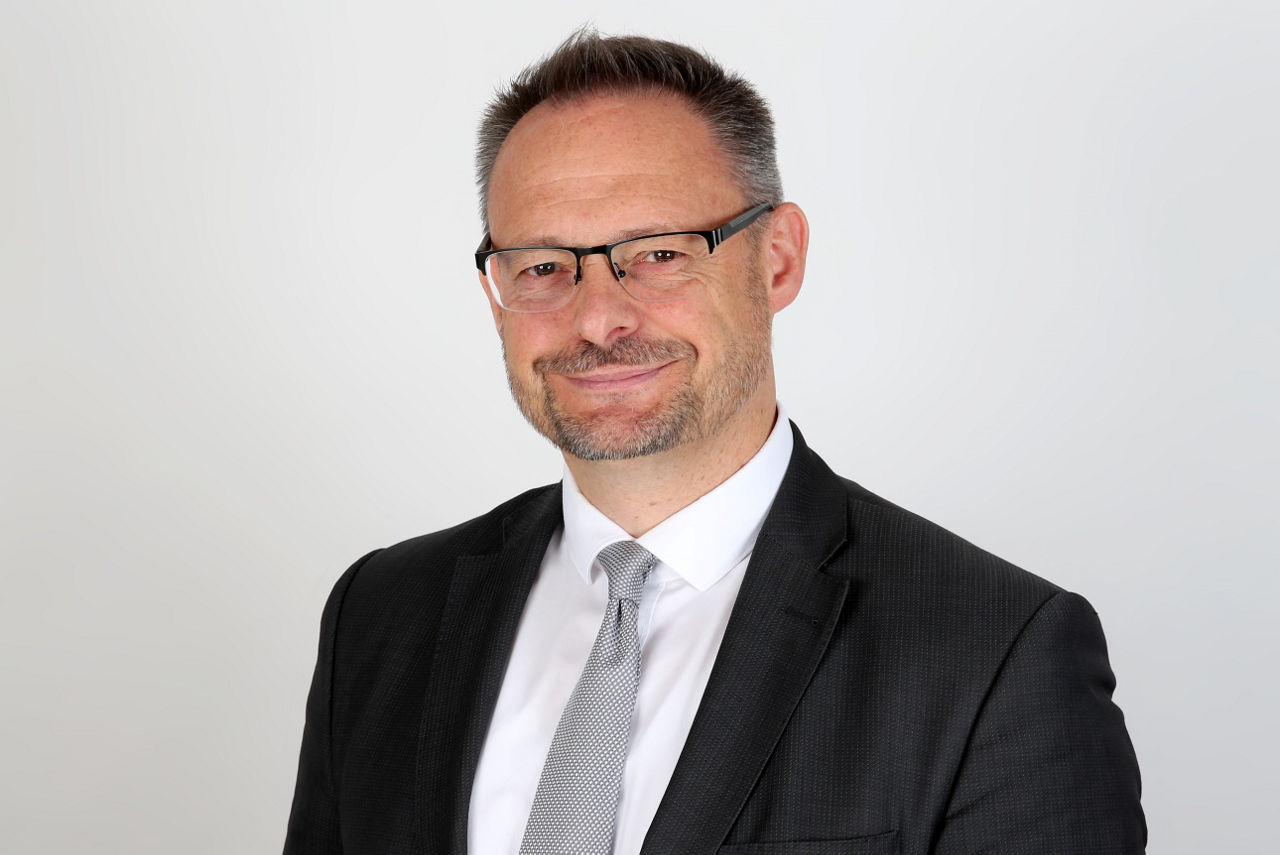 Ein lächelnder Mann in einem Anzug schaut in die Kamera.